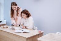 Two women collaborating on a study project in a classroom environment.