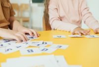 Children arranging alphabet cards on a yellow table in a classroom setting.