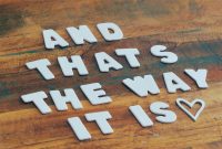 Inspirational message 'And That's The Way It Is' in wooden letters on a rustic wooden table.